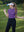 Model in purple women's performance solid polo holding a golf club outdoors