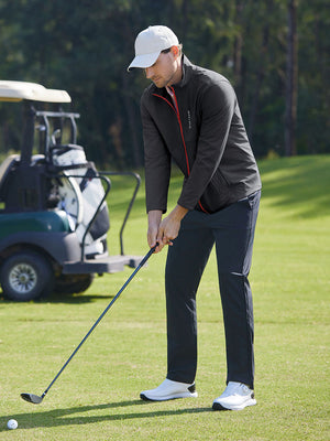 Model in dark grey softshell water resistant lightweight jacket preparing to tee off, full-body shot