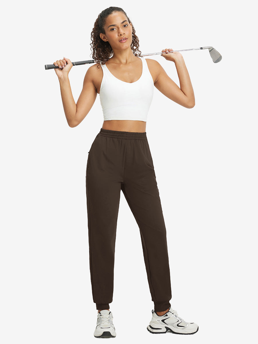 Model holding golf club behind neck while wearing lightweight women's stretchy joggers sweatpants in coffee brown.