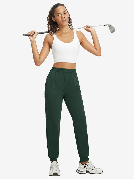 Model holding golf club behind neck while wearing lightweight women's stretchy joggers sweatpants in forest green.
