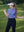 Model in haze blue women's performance solid polo holding a golf club outdoors