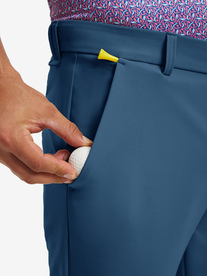 Hand placing a golf ball into pocket of water-resistant golf stretch nylon pants in blue indigo.