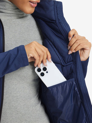 Hand placing an iPhone into pocket of women's lightweight fleece-lined puffer jacket in navy.